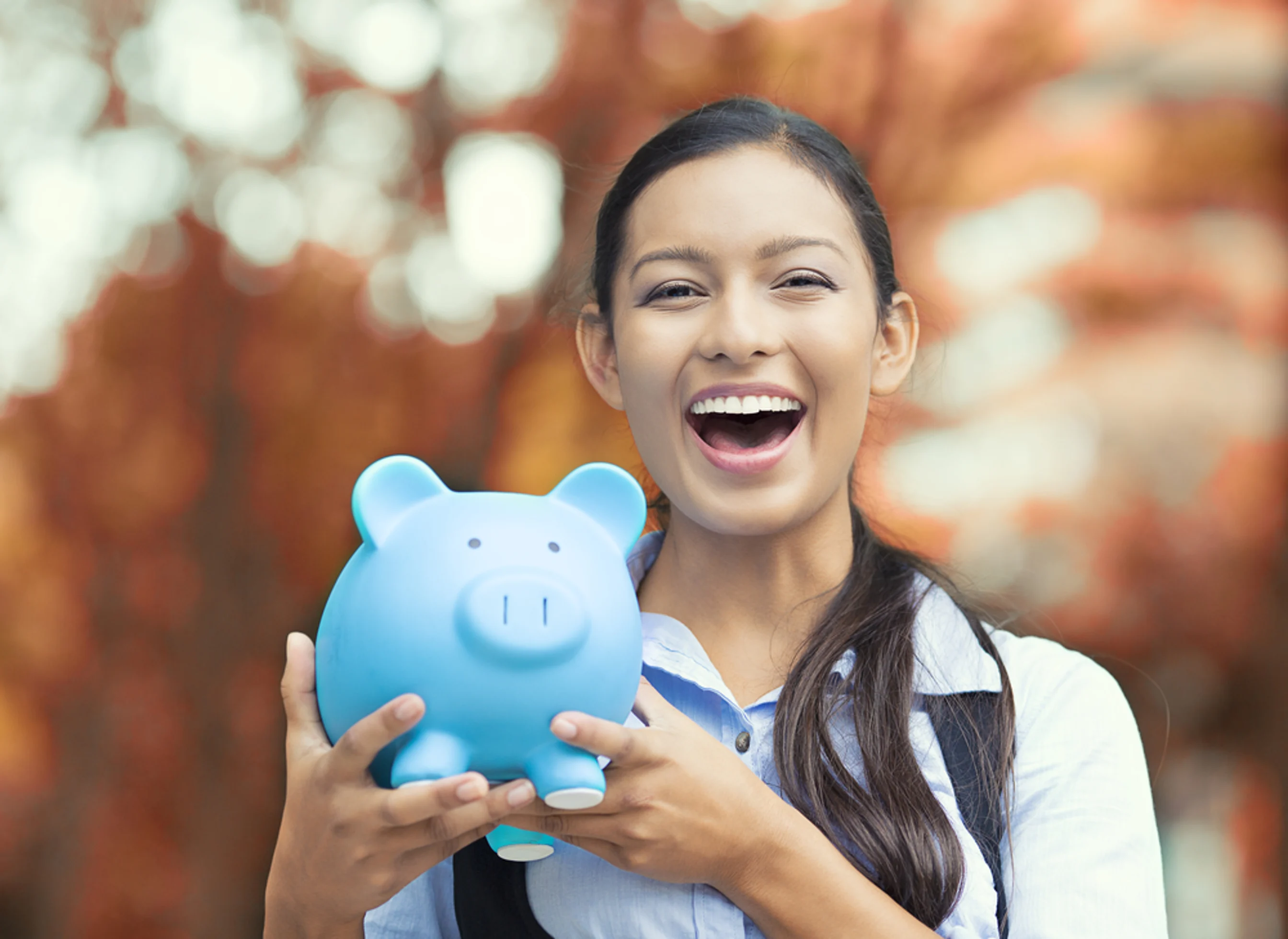 Closeup portrait happy smiling business woman bank employee holding piggy bank isolated outdoors indian autumn background Financial savings banking concept Positive emotions face expressions
